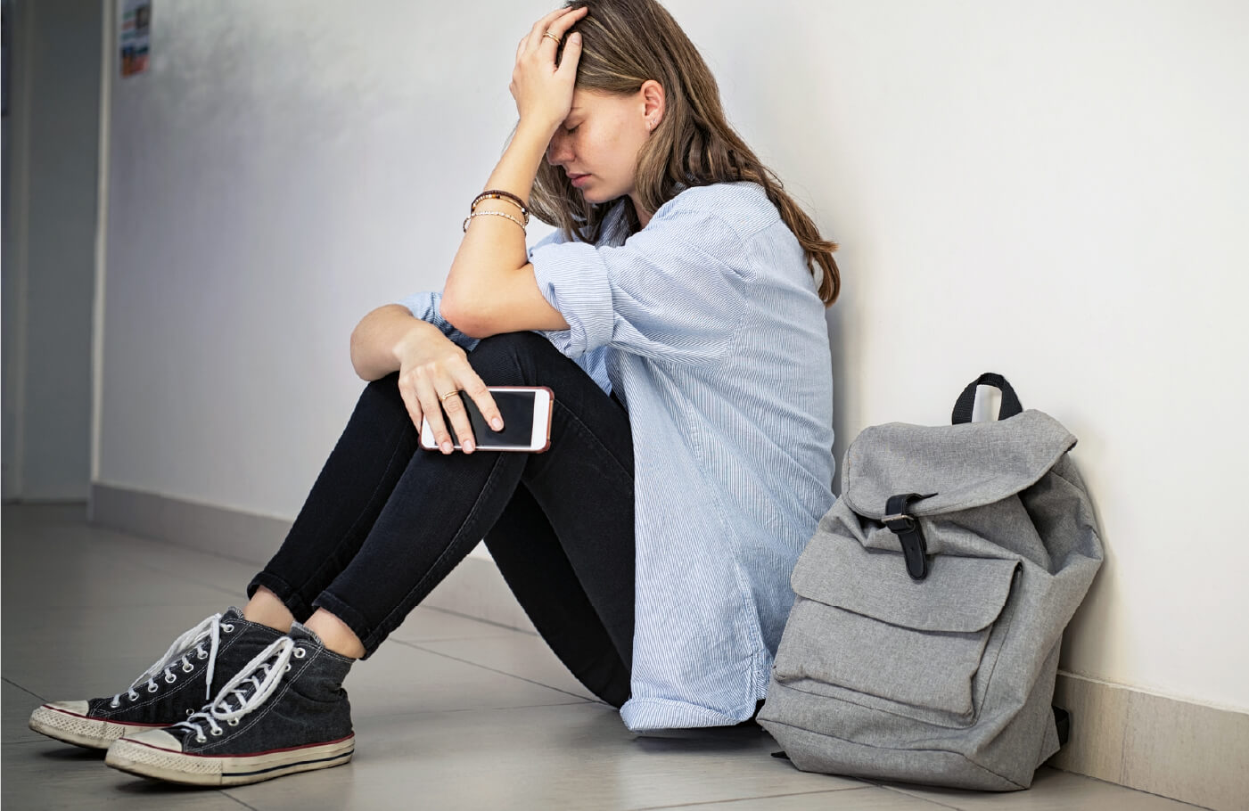 A seated teen girl leaning against a wall with her hand on her head.