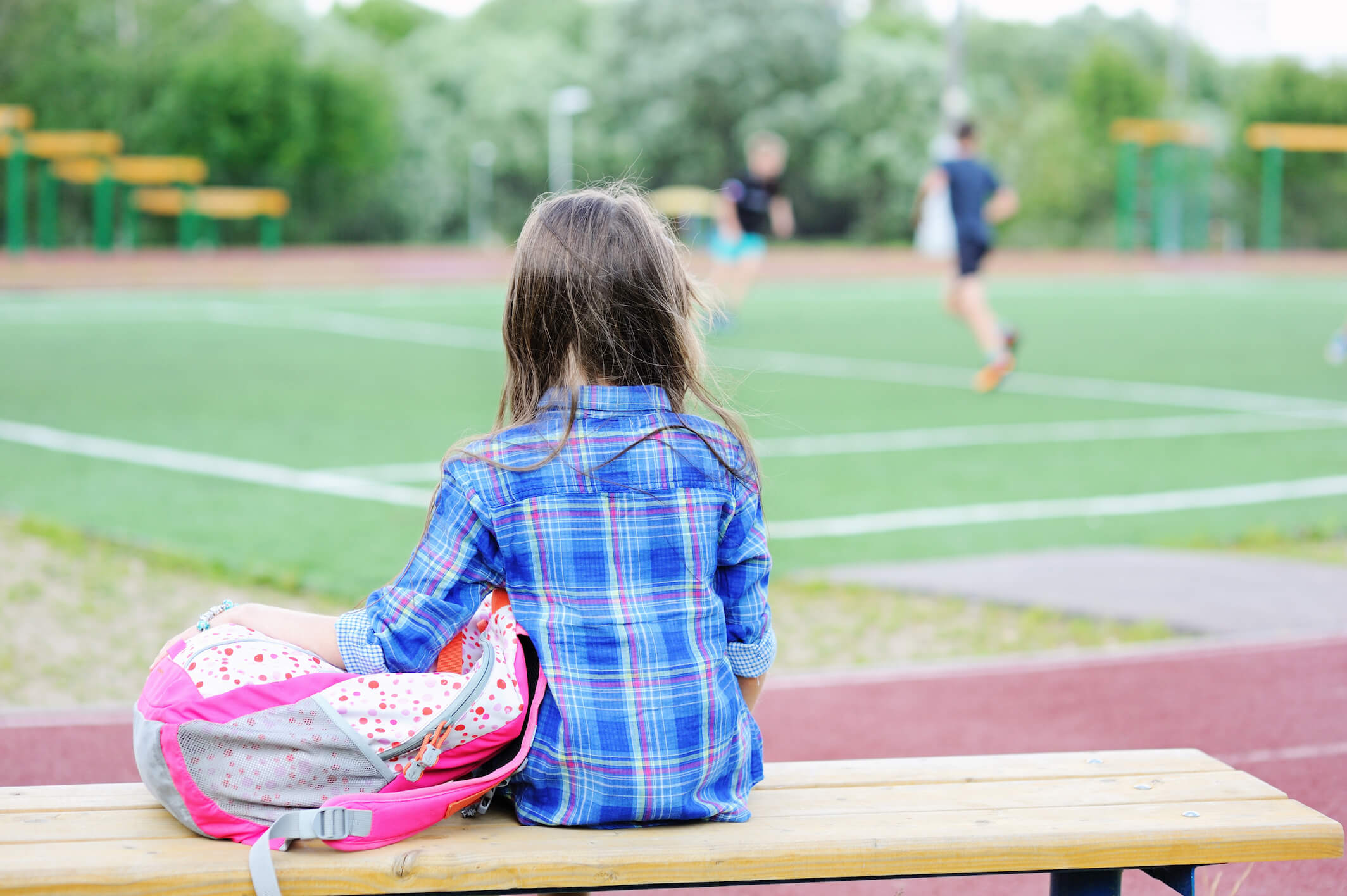 Girl sitting alone on a bench at a soccer game.