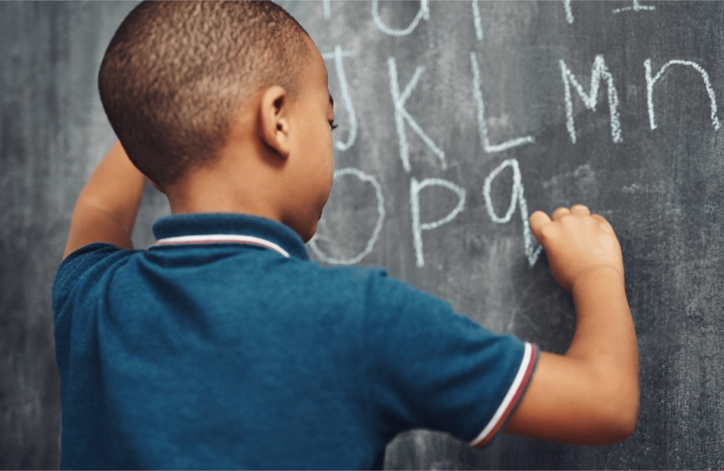 Boy in a blue shirt writing the alphabet on a chalkboard.