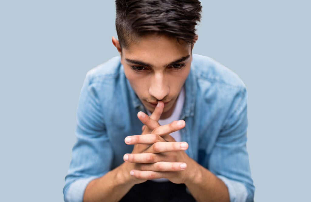 Teen boy is pensively looking down with his fingers interlocked.