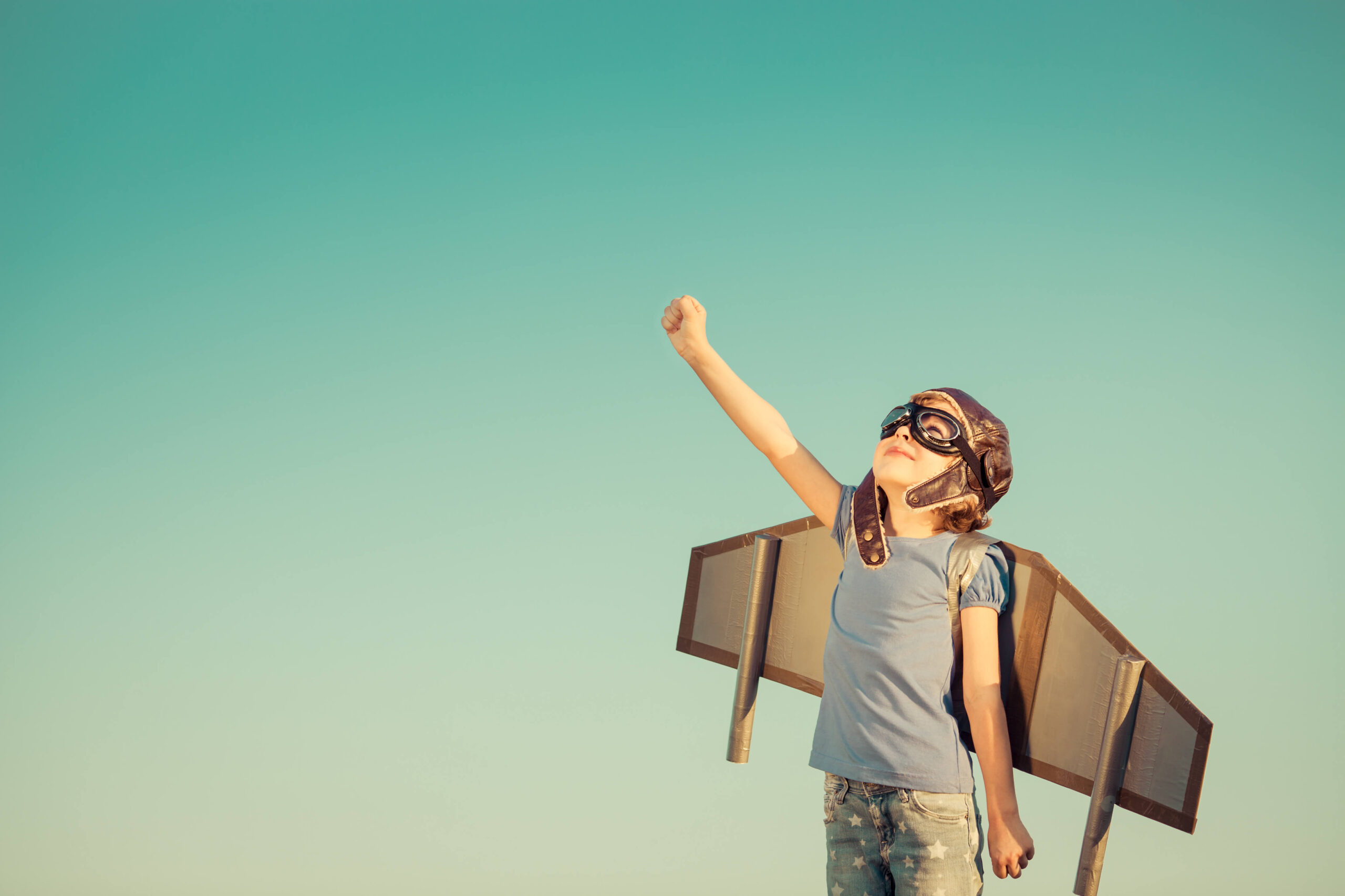 Child wearing pilot helmet and homemade plane costume with arm raised.