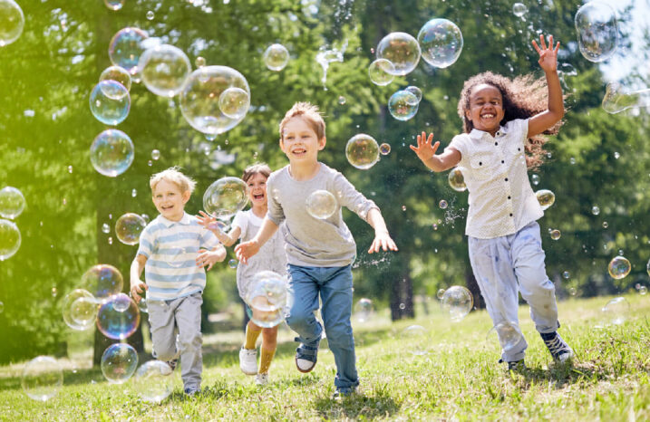 A group of children in an open field running towards bubbles.