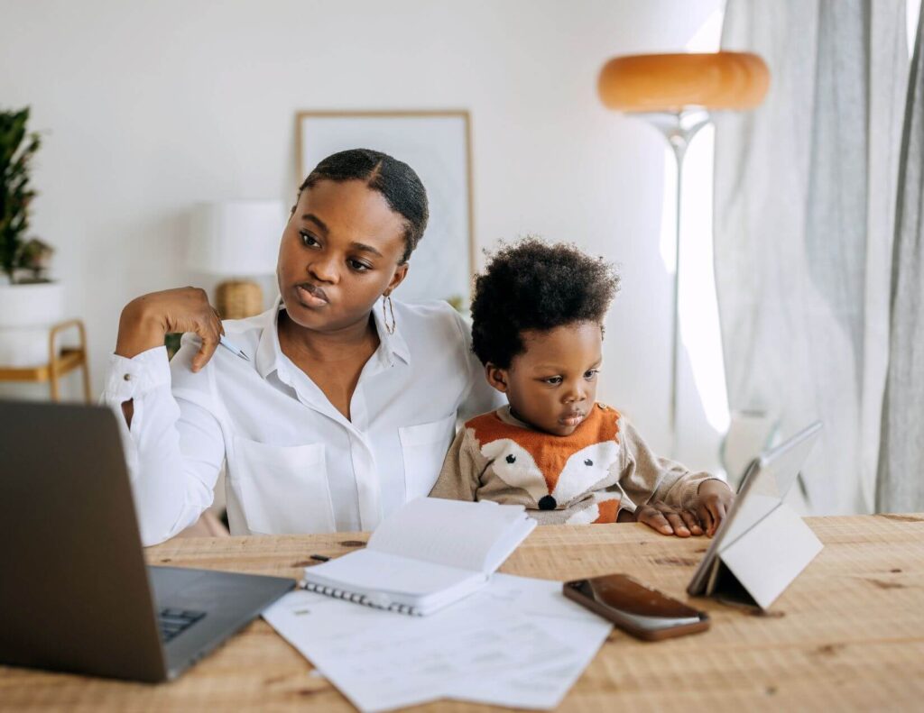 Busy mom multitasking by working on her computer while holding her toddler.