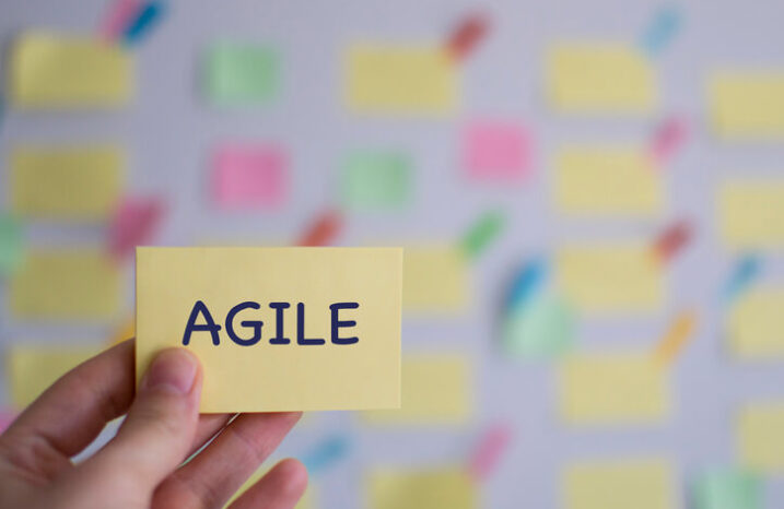 Hand holding a yellow piece of paper with the word agile on it.