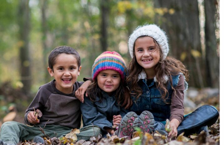 Three children sitting and smiling on a beautiful autumn day.
