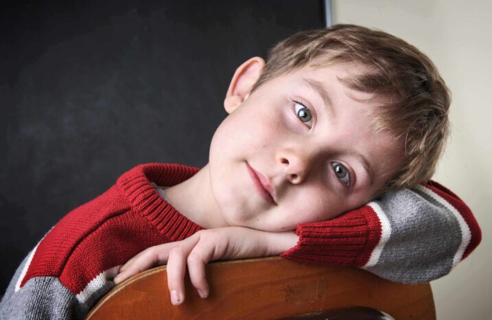 Young boy peacefully resting his head on his arm while sitting in a chair.
