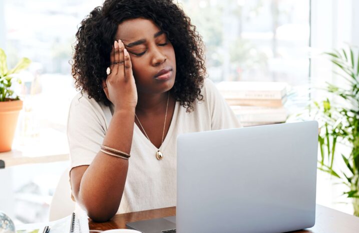 Woman sitting at her laptop with her eyes closed and her hand on her face.